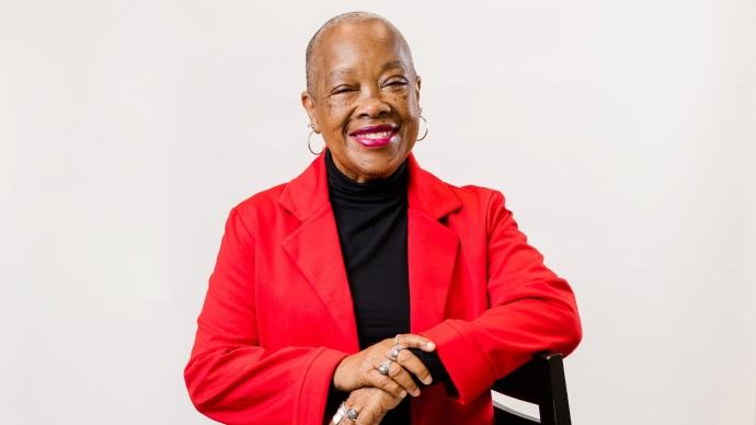 A portrait of Valerie Bridgeman '86 wearing a red blazer, leaning on a chair, and smiling