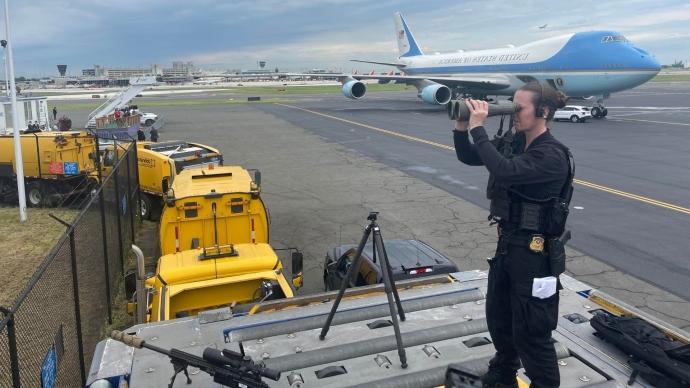 Kim Sayles uses binoculars while st和ing guard at the Air Force 1 runway